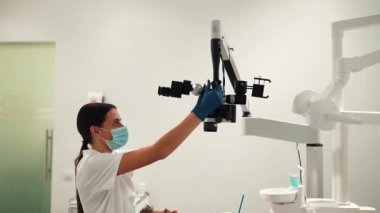 Kadın bir dişçi dişlerine bakan genç bir hastayı dişçi odasında profesyonel bir mikroskop ile muayene ediyor. Diş işleten mikroskop. Diş optiği.