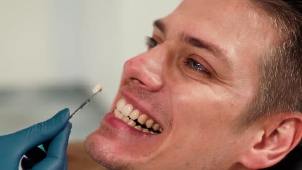 医療の概念 歯の色のサンプルを持つ歯科医の閉鎖歯科クリニックで男性患者の歯のための日陰を選択します — ストック動画