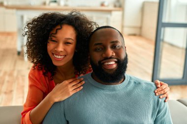 Afro-Amerikalı çift kanepede oturuyor ve evlerinde birbirlerine sarılıyorlar..