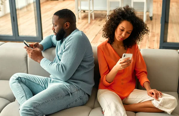 アフリカ系アメリカ人のカップルがソファに座り 自宅のリビングルームで電話が顔を合わせています — ストック写真