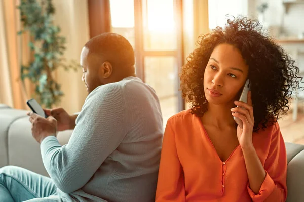 アフリカ系アメリカ人のカップルがソファに座り 自宅のリビングルームで電話が顔を合わせています — ストック写真