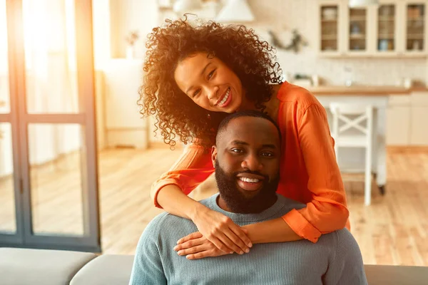 アフリカ系アメリカ人の夫婦はソファに座って自宅のリビングルームで抱き合って — ストック写真