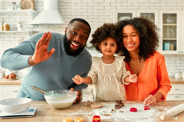 キッチンで楽しさと料理のペストリーを持っている巻きふわふわの髪を持つ小さな娘とアフリカ系アメリカ人の家族 お父さんとお母さんと娘が一緒に調理し 生地からクッキーを切り取る — ストック写真