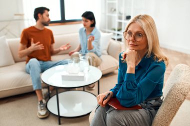 Mutsuz çift tartışıyor, tartışıyor, psikolog ofisinde anlaşmazlık yaşıyor, genç ailenin terapistleriyle ilişki sorunlarını tartışıyor..