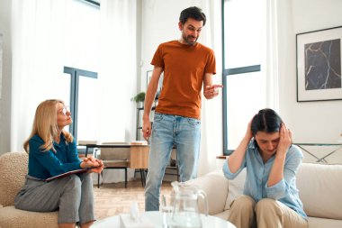 Mutsuz çift tartışıyor, tartışıyor, psikolog ofisinde anlaşmazlık yaşıyor, genç ailenin terapistleriyle ilişki sorunlarını tartışıyor..