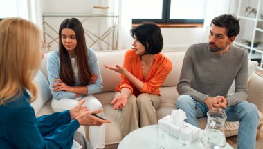 Psikolog randevusunda ailesiyle birlikte üzgün bir genç kız. Aile psikoloji seansında. Genç çocukların sorunlarını çözmek için genç bir aileye yardım eden psikolog..