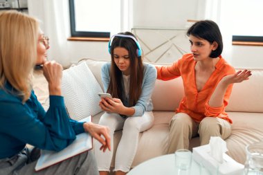 Ebeveynlerin psikolojik sorunları. Genç kız kulaklıkla müzik dinlerken ve akıllı telefon kullanırken psikolog sosyal hizmet görevlisi annesiyle konuşuyor. Aile terapisi. Sosyal ağlarda sorun.