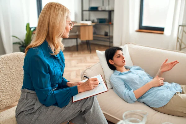 Psychological trauma. Female psychologist aged working with a depressed woman in the office, the patient lies on the couch during a session with a therapist.