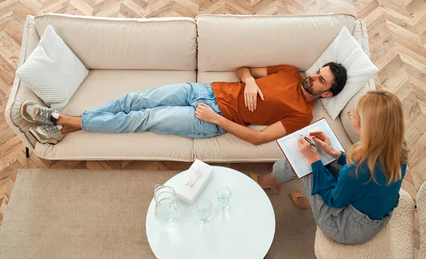 Young depressed man at the reception of a female psychologist during a mental health session lying on the couch. A man in frustrated feelings at a psychologist, being in a state of stress.