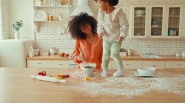 Kıvırcık saçlı ve mutfakta kurabiye yapan küçük kızı olan Afro-Amerikalı bir kadın. Anne ve kızı birbirlerini un ile kirletip oynuyorlar..