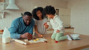 Kıvırcık saçlı ve mutfakta hamur işi pişiren küçük kızları olan Afro-Amerikan bir aile. Baba, anne ve kız birlikte yemek pişiriyor ve hamurdan kurabiye kesiyorlar..