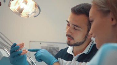Male Dentist shows the patient an artificial model of the jaw with braces. How to properly care for your oral cavity, put braces, cost and consequences