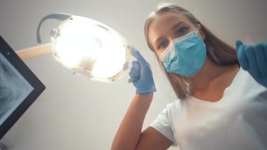 Young beautiful caucasian doctor dentist moves the lamp to examine the patient's oral cavity.