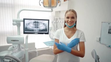 Beautiful young smiling doctor dentist woman crosses her arms while standing in the dental office.