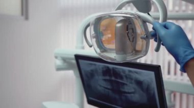 Close up shot of the dentist's hand moves dental lamp. The man moves a dental lamp closer to the patient's chair.