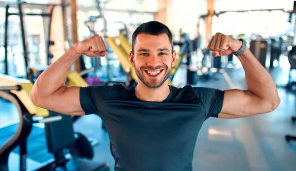 Kas yığını bir adam spor salonundaki spor malzemelerinin arka planında dururken kollarındaki kaslarını, gücünü ve gücünü gösterir. Aktif sağlıklı yaşam tarzı, spor.
