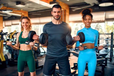 Young multi-ethnic group of people wearing sportswear doing exercises with dumbbells in a gym club. The concept of sports and recreation.