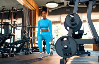 Spor giyimli, narin Afrikalı Afrikalı Amerikalı bir kadın spor salonunda halterlerle egzersiz yapıyor. Spor ve eğlence kavramı..