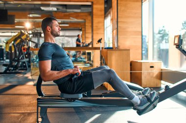 Spor giyim bölümündeki kaslı genç adam spor salonunda simülatör üzerinde egzersiz yapıyor. Spor ve eğlence kavramı..