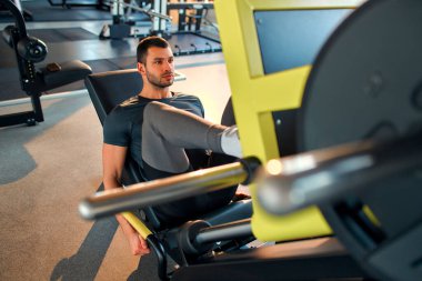 Spor giyim bölümündeki kaslı genç adam spor salonunda simülatör üzerinde egzersiz yapıyor. Spor ve eğlence kavramı..