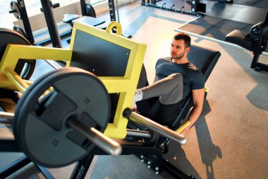 Spor giyim bölümündeki kaslı genç adam spor salonunda simülatör üzerinde egzersiz yapıyor. Spor ve eğlence kavramı..