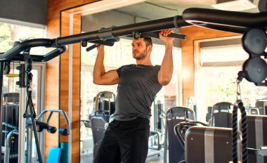 Spor giyimli beyaz kaslı adam spor salonunun yatay çubuğuna yanaşıyor. Spor ve eğlence kavramı..