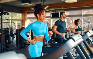 A group of multiethnic young people running on a treadmill in the gym. Cardio workout. The concept of sports and recreation.
