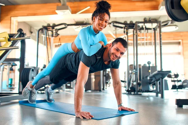 Spor salonunda sırtüstü yatan Afrikalı Amerikalı bir kadınla lastik minder üzerinde tahta egzersizi yapan kaslı atletik bir adam. Atletik genç çift. Spor ve eğlence kavramı..