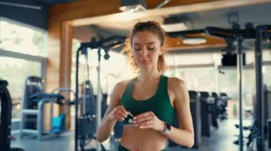 Slender caucasian woman in sportswear putting on wireless headphones while standing in the gym. Active healthy lifestyle, sport.
