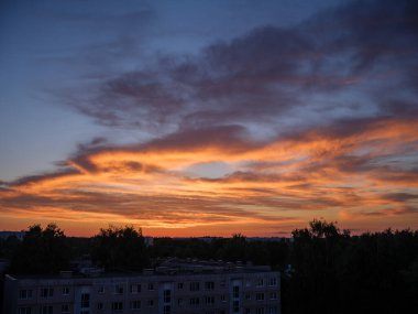 Şehrin çatıları üzerinde dramatik kırmızı ve koyu mavi bulutlar. Şehir silüeti.