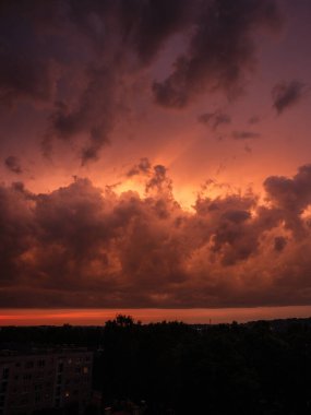 Şehrin çatıları üzerinde dramatik kırmızı ve koyu mavi bulutlar. Şehir silüeti.