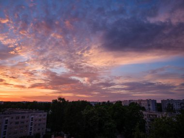 Şehrin çatıları üzerinde dramatik kırmızı ve koyu mavi bulutlar. Şehir silüeti.