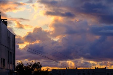 Şehrin çatıları üzerinde dramatik kırmızı ve koyu mavi bulutlar. Şehir silüeti.