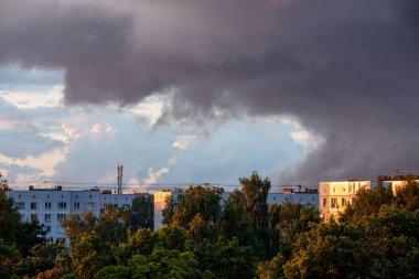 Şehrin çatıları üzerinde dramatik kırmızı ve koyu mavi bulutlar. Şehir silüeti.