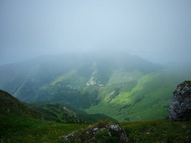 Slovenya Triglav Ulusal Parkı 'ndaki puslu dağların tepeleri. Kayalar ve yeşil çayırlar ile yaz manzarası.
