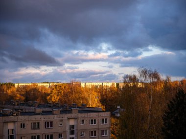 Şehrin çatıları üzerinde dramatik kırmızı ve koyu mavi bulutlar. Şehir silüeti.