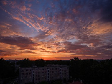 Şehrin çatıları üzerinde dramatik kırmızı ve koyu mavi bulutlar. Şehir silüeti.