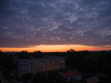 Şehrin çatıları üzerinde dramatik kırmızı ve koyu mavi bulutlar. Şehir silüeti.