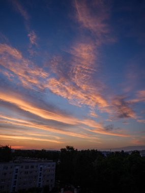 Şehrin çatıları üzerinde dramatik kırmızı ve koyu mavi bulutlar. Şehir silüeti.