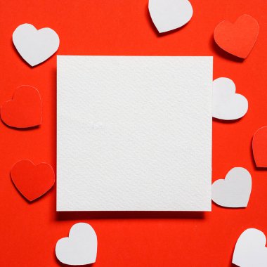 Kırmızı zemin üzerine boş kare kağıt, kırmızı arka planda küçük bir kalp şeklinde kesilmiş kırmızı ve beyaz kağıt, Sevgililer Günü için tebrik kartı fikirleri.