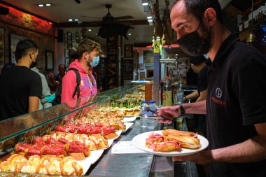 San Sebastian, İspanya; 27 Ekim 2021: Tipik pintxo bar ve Jabugo jambonu asma. Covid-19 salgınının son darbeleri, kurumların içinde işaretleri olan insanlar. Yeni gerçeklik.
