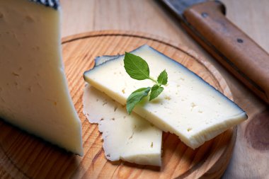 Kesme tahtasının üzerinde yarı pişmiş İspanyol peyniri parçaları.