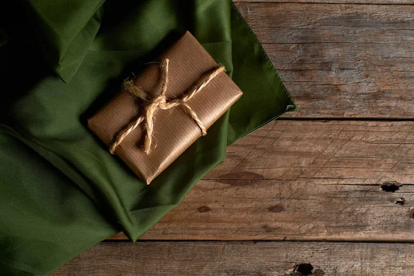 Kahverengi kraft kağıdına sarılı kutu ve iple bağlanmış yeşil ipek kumaş ve kırsal ahşap masa