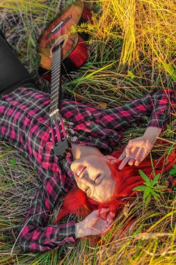 Çimlerin üzerinde gitarla yatan güzel genç bir kadın. Sonbahar günü
