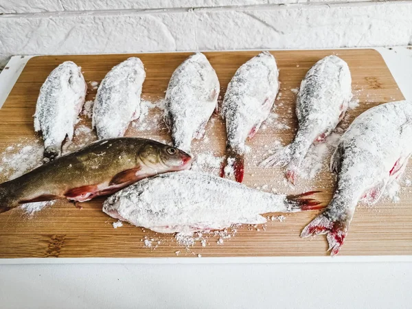 Kesme tahtasındaki un içinde nehir balığı, dekoratif bir duvarın arka planında.