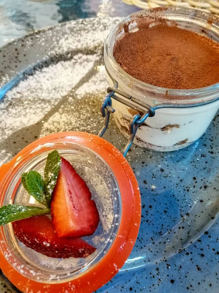 Mavi bir tabakta, pudra şekeri serpiştirilmiş, fincanda tiramisu keki ve naneli taze çilek dilimleri..