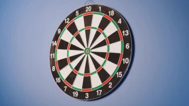 Dart oyunu. Hedefe dart atıyorlar. Ve birisi dart tahtasına dart atabilir. Mavi arka planda asılı bir dart tahtası.