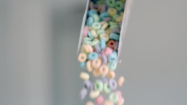 Los cereales de desayuno en forma de anillos de maíz de colores se vierten fuera del paquete. Comida de cerca: copos de maíz coloreados y productos lácteos. Movimiento lento. — Vídeo de stock