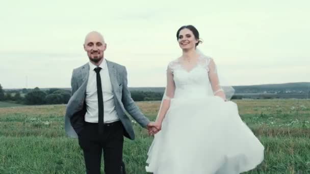 Frisch verheiratet. Schöne junge Braut und Bräutigam laufen auf das Feld. Ein Hochzeitspaar. Glückliche Familie. Ein Mann und eine Frau, die ineinander verliebt sind. Die Braut in einem wunderschönen — Stockvideo