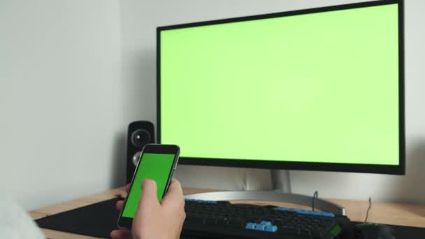 Close-up van een man met behulp van een smartphone groen scherm op een tafel met een computer Chromakey. Een close-up van mannelijke handen met een groen scherm voor mobiele telefoons.. — Stockvideo